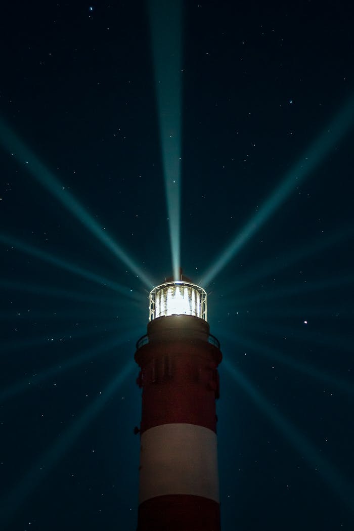 A lighthouse casts beams of light into the starry night sky, providing a stunning navigational landmark.
